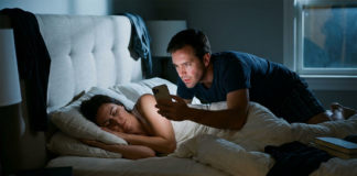 眠っている妻の顔にiPhoneをかざしてロック解除しようとしている夫